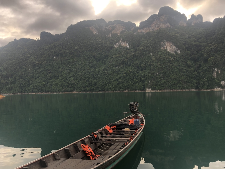 Longtail boat on a calm lake surrounded by mountains.
