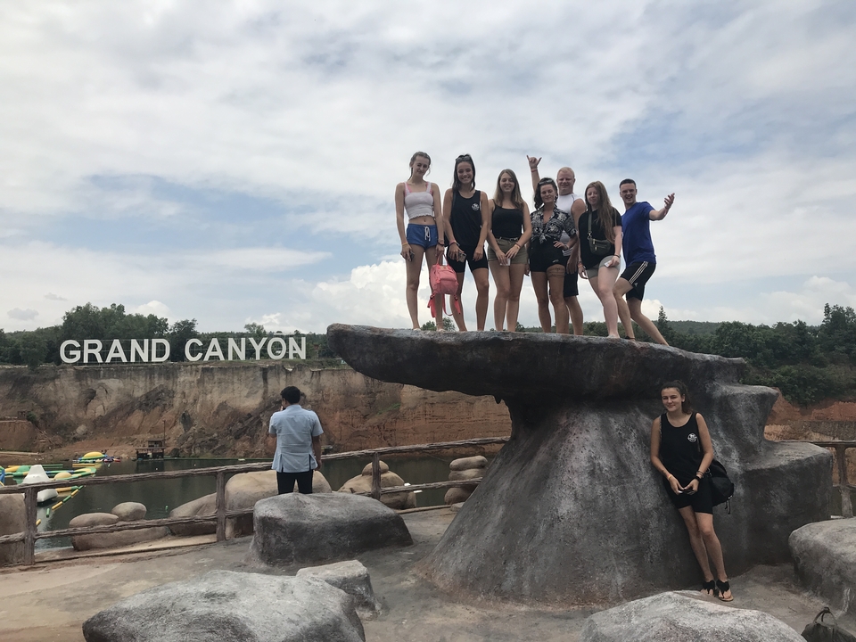 A group of people posing over a rock with 'GRAND CANYON' in the background.