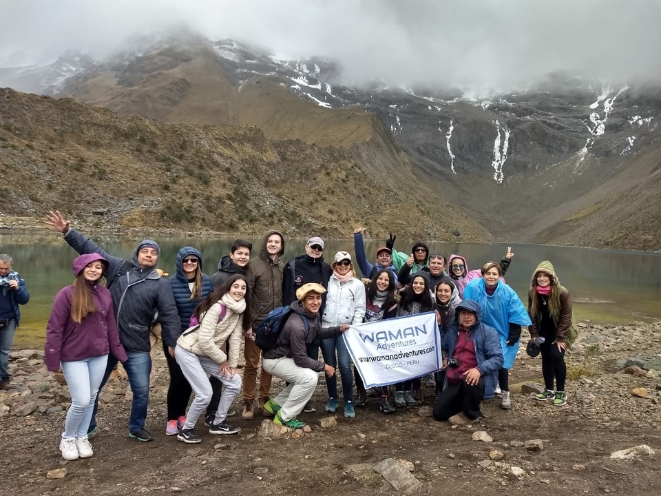 Group posing with a banner by a lake in mountainous scenery.