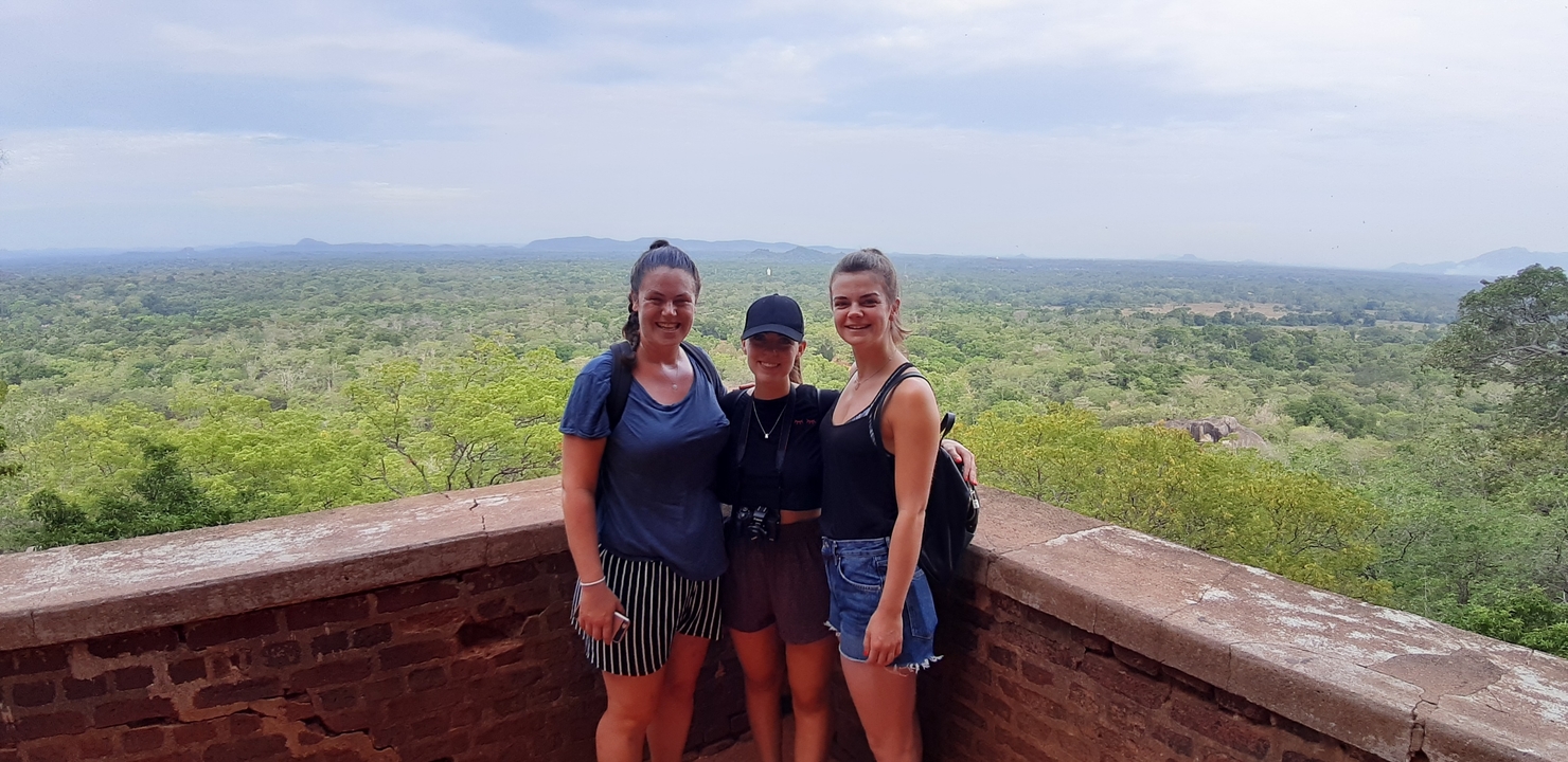Three women posing with a scenic valley backdrop.