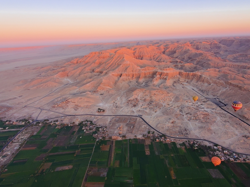 Aerial view of mountains and desert at sunrise with hot air balloons.