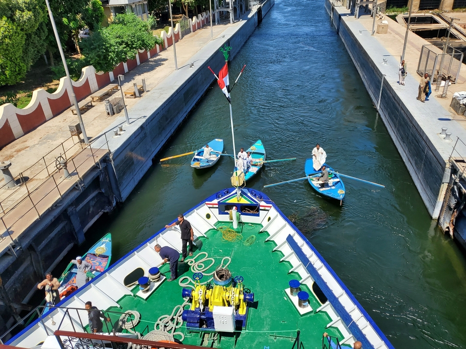People navigating boats through a canal with a large flag.