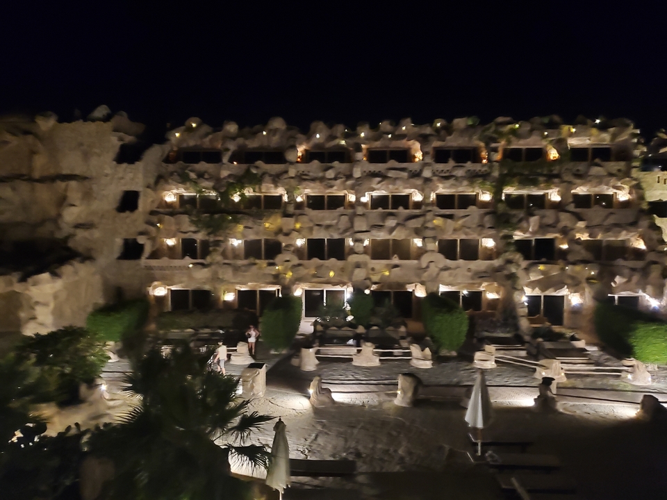 Hotel facade at night with lights and greenery.