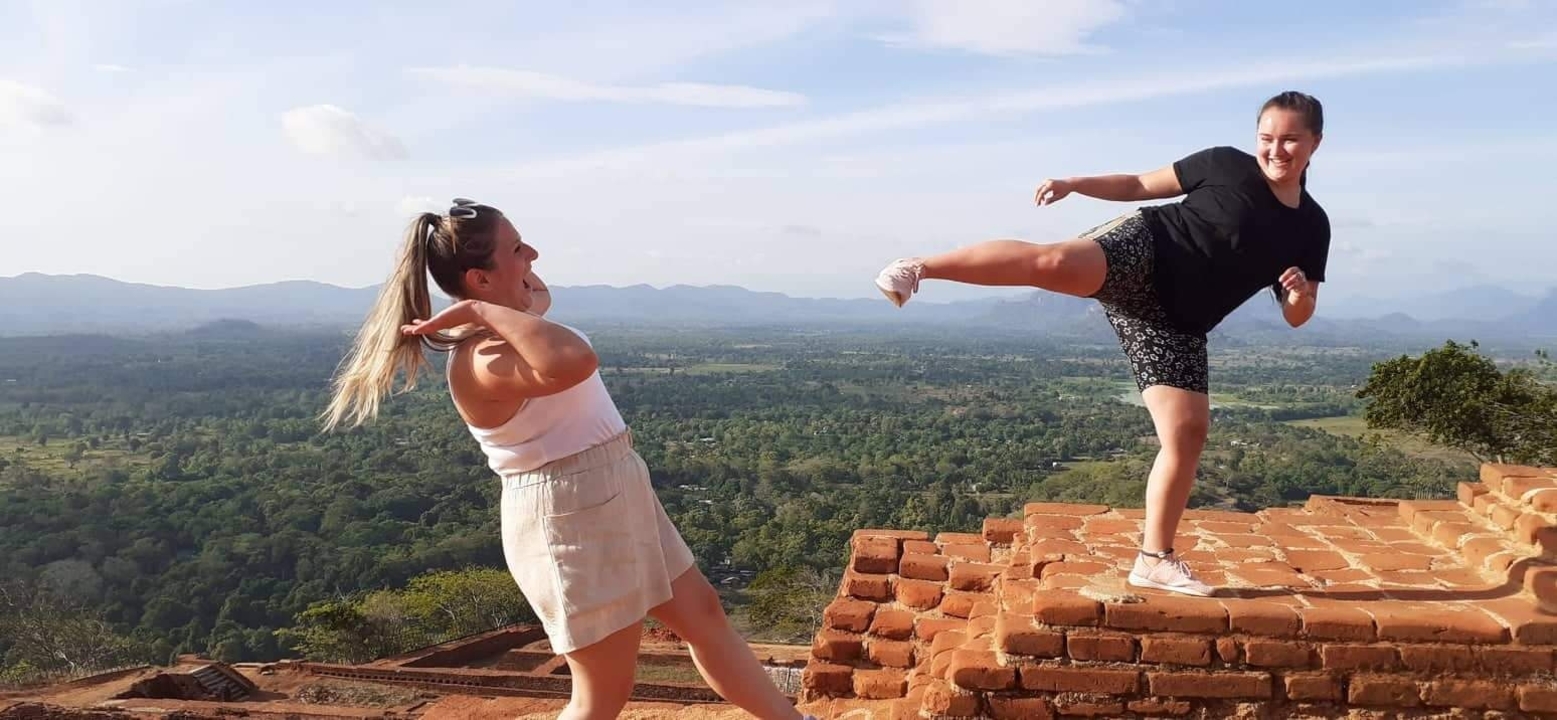 Two women playfully posing with scenic views from a brick structure.
