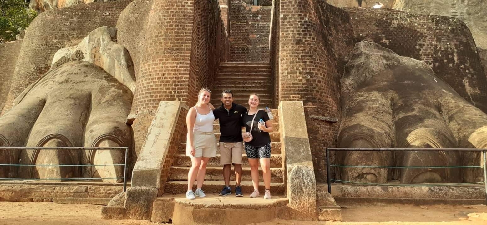 Tourists posing at the entrance of a historic site with large lion paws.