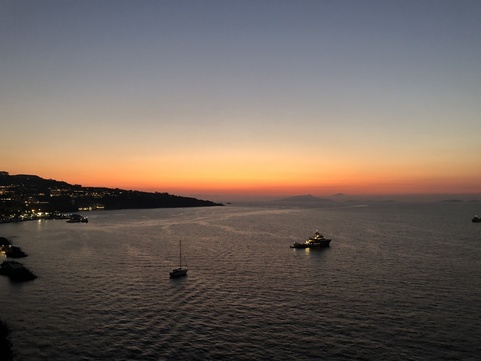 Sunset over a calm sea with boats silhouetted.