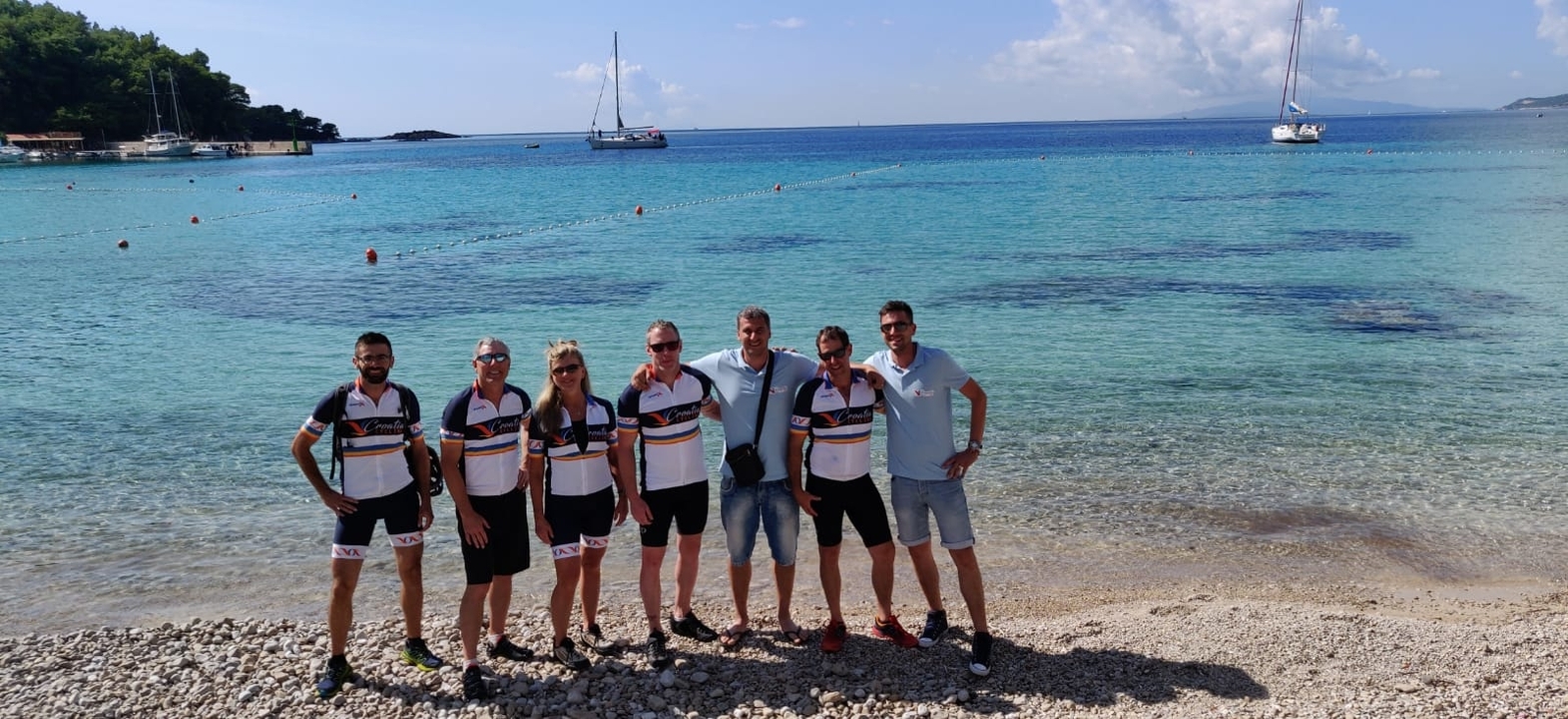Group of cyclists posing on a pebble beach with calm sea in the background.