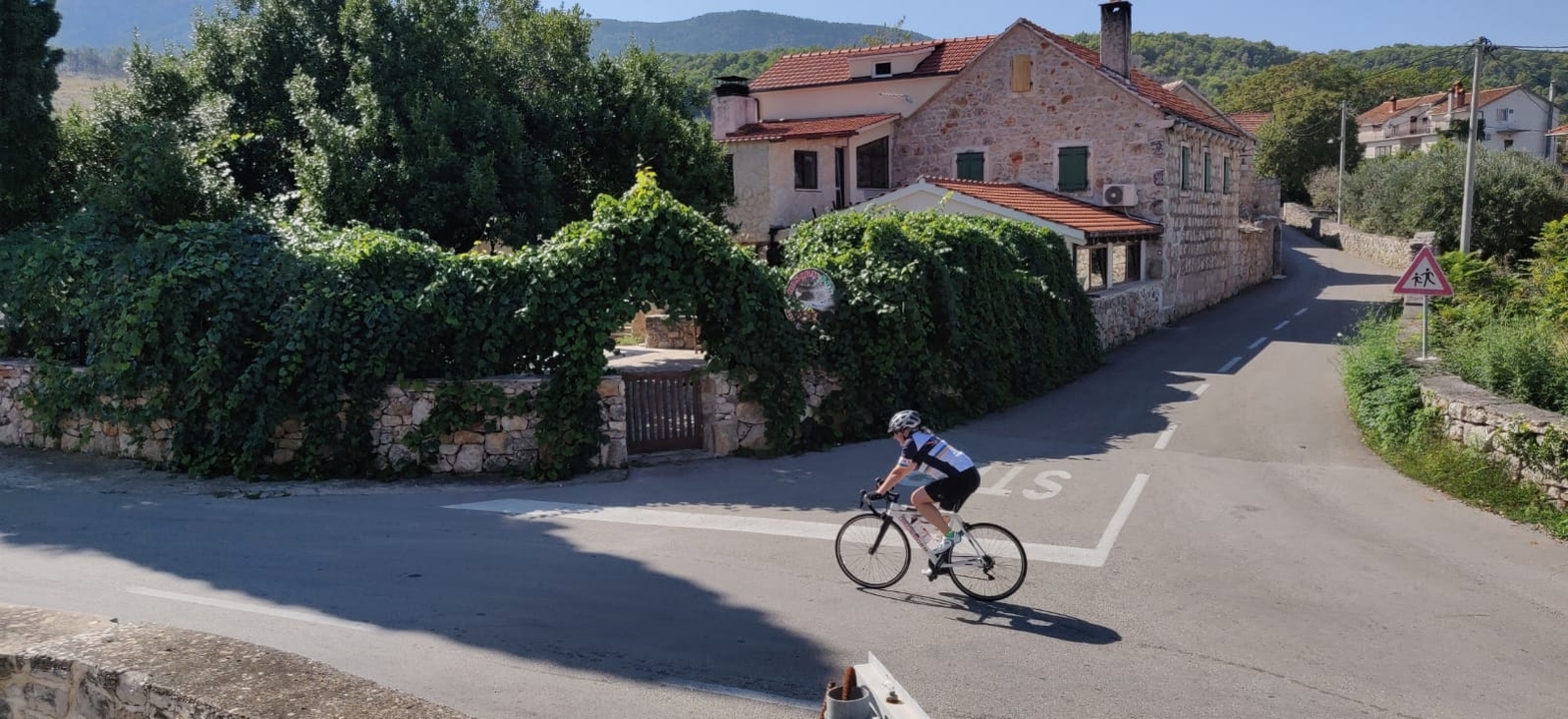 Cyclist riding through a village with vine-covered walls.
