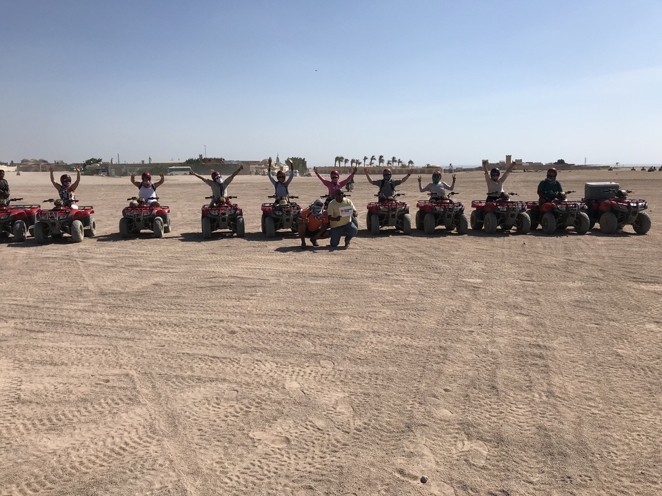 People on quad bikes in a desert landscape, raising their hands.