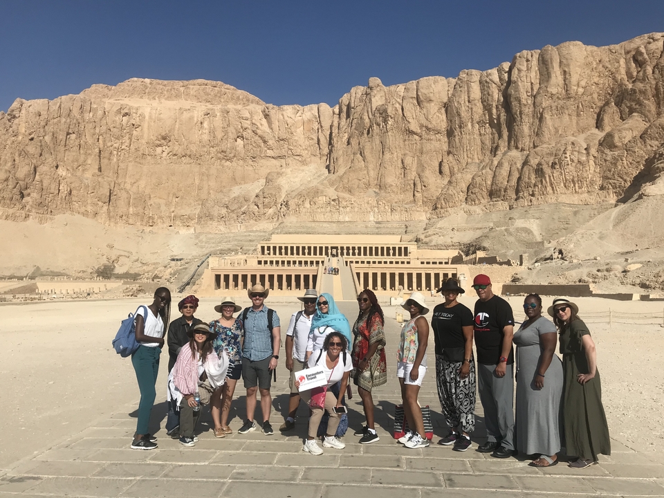 Group of people in front of the Temple of Hatshepsut in a desert landscape.