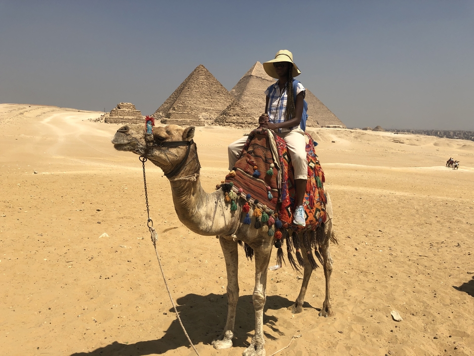 Person riding a camel near pyramids in the desert.