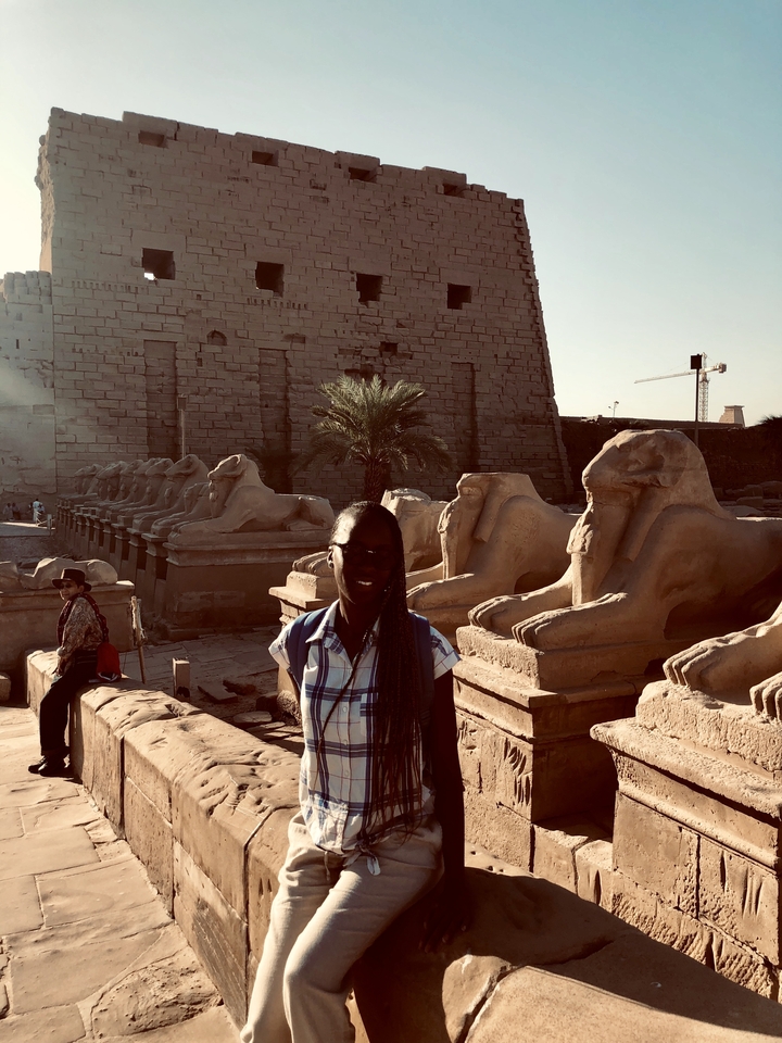 Person posing in front of rows of stone sculptures at Luxor Temple.