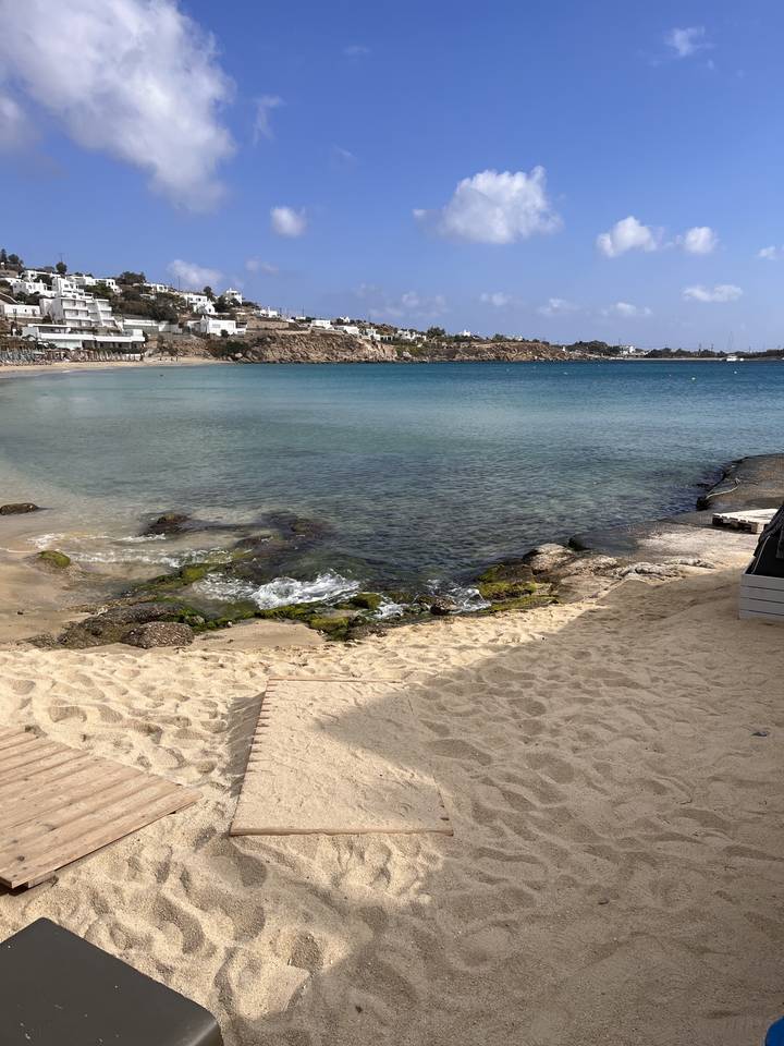 Sandy beach with clear waters and buildings in the distance.