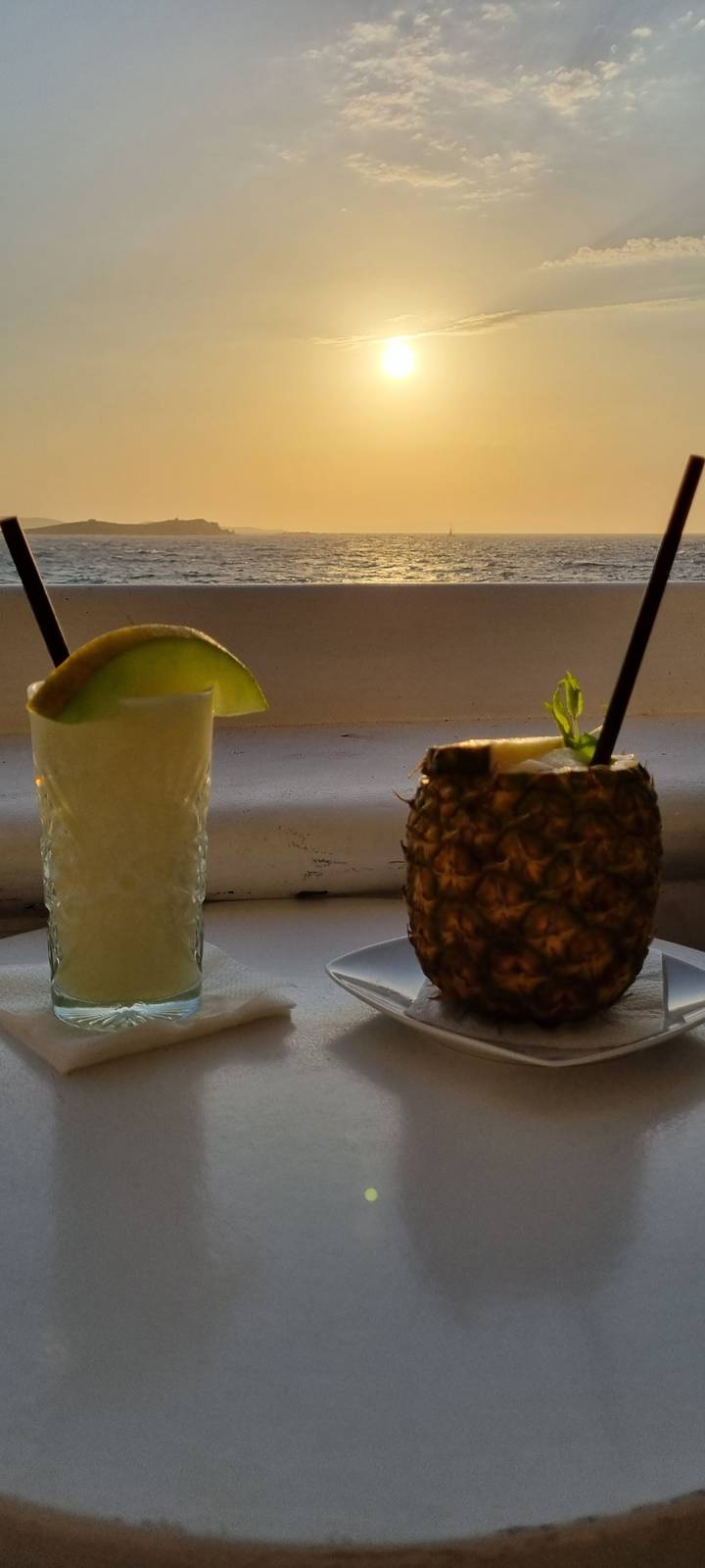 Two cocktails with one in a pineapple, set against a sunset.