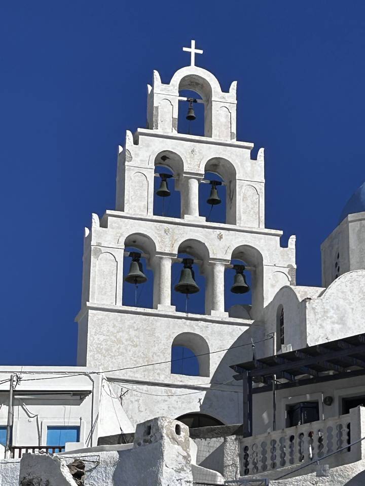 Side view of a multi-bell tower against a clear blue sky.
