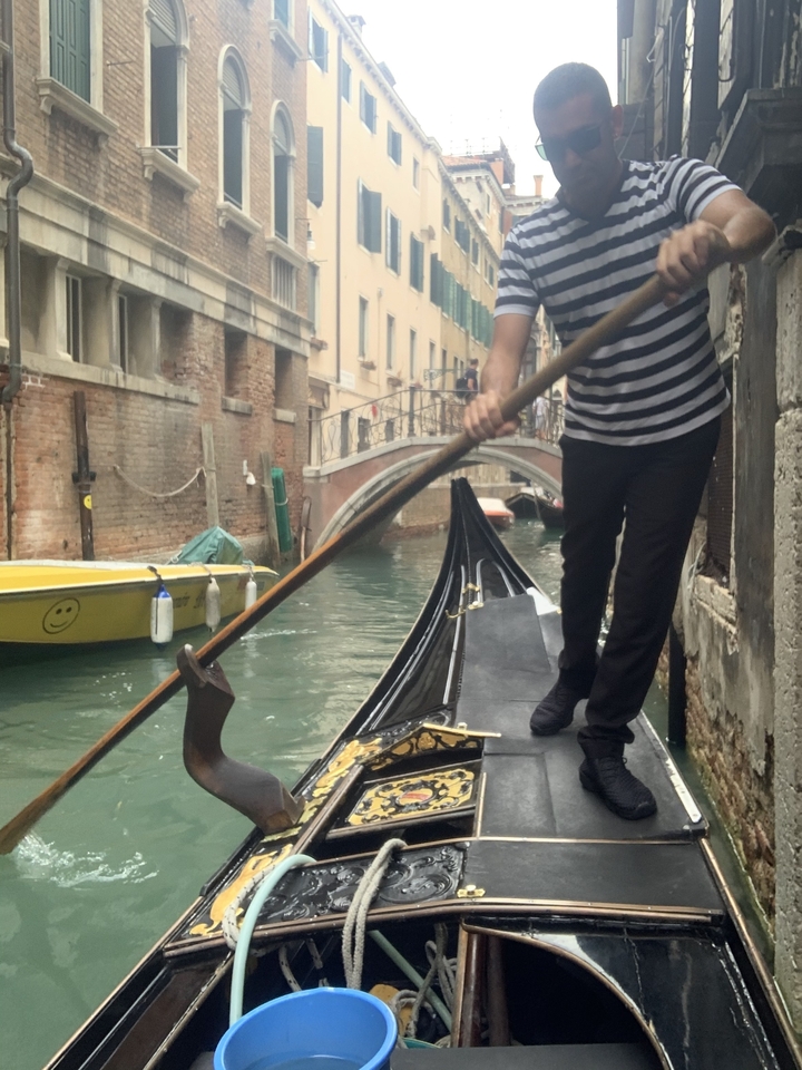 Gondolier manœuvrant une gondole dans un canal étroit de Venise.