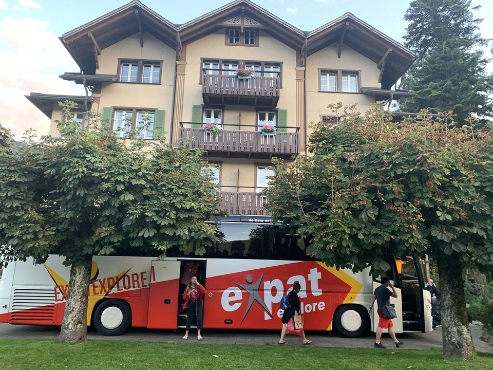 Autocar touristique garé près d'un hôtel avec des gens aux alentours.