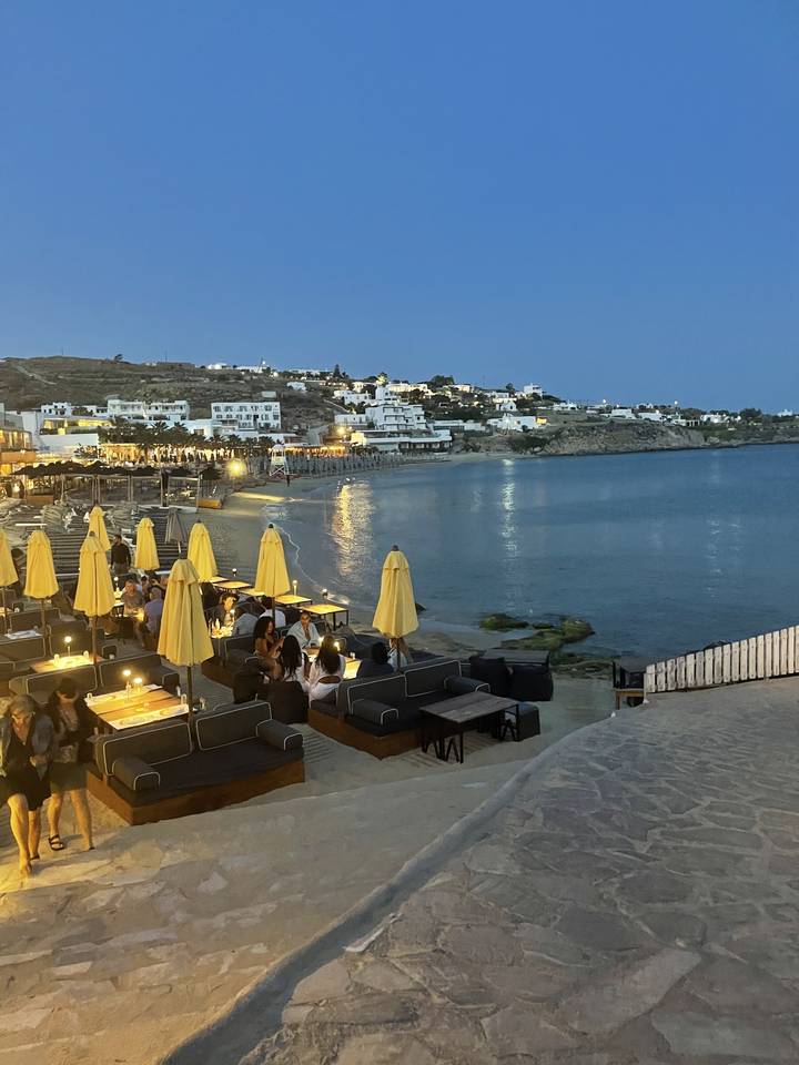 Outdoor seating by the water at dusk with buildings in background.