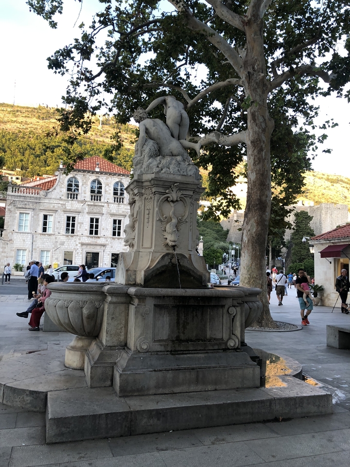Des gens près d'une fontaine en pierre avec l'architecture environnante.