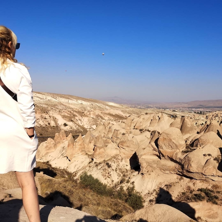 A woman overlooking a rocky landscape with hot air balloons in the sky.