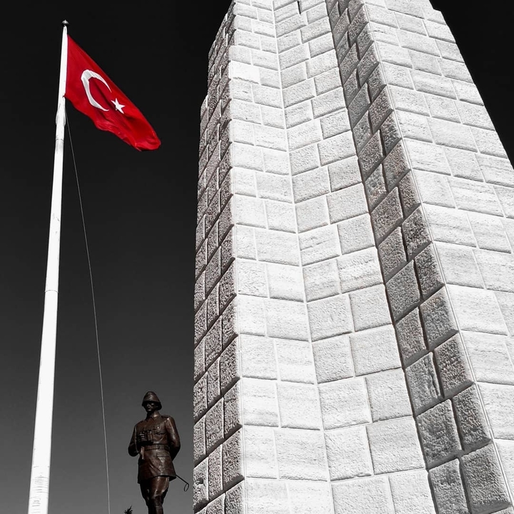 A monument with a red Turkish flag against a blue sky.