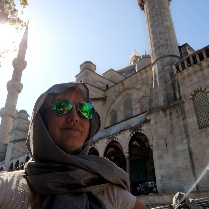 A woman wearing sunglasses in front of an ornate mosque.