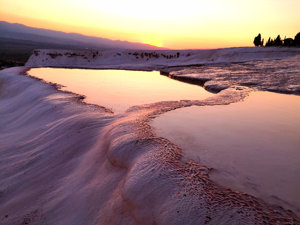 Sunset over Pamukkale terraces reflecting the orange sky.