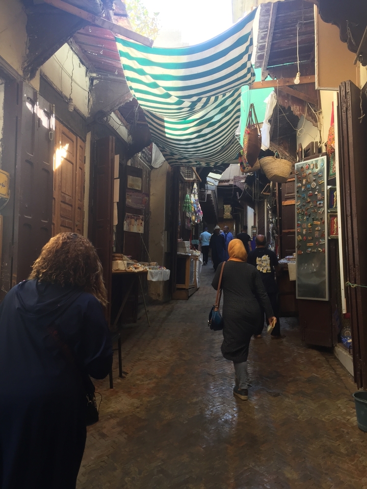 A busy market street with people shopping, surrounded by colorful merchandise.