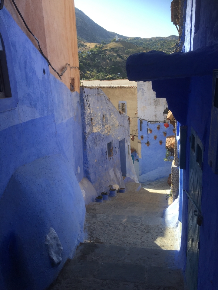 A narrow alley with vivid blue walls and pottery hanging on the wall, typical of Chefchaouen.