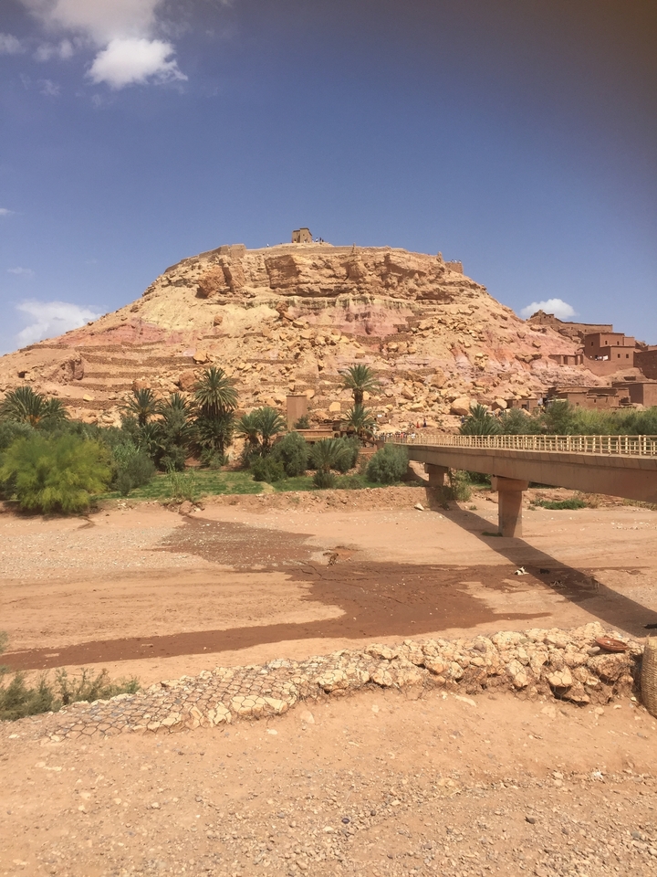 A historic fortified village with a river and a bridge in the foreground.