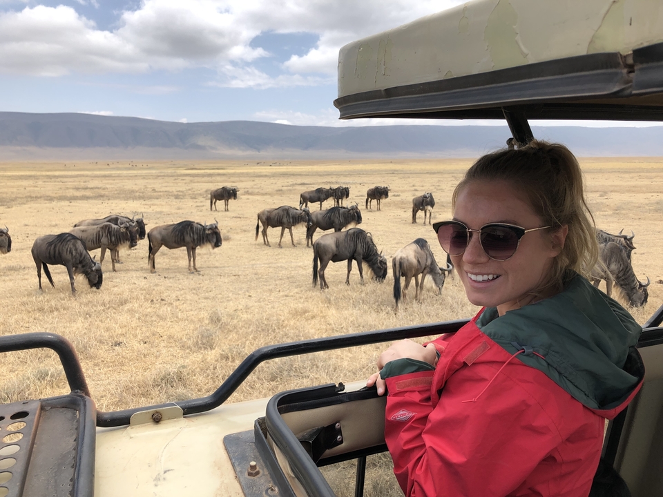 Femme souriante dans une jeep de safari avec des gnous qui paissent en arrière-plan.