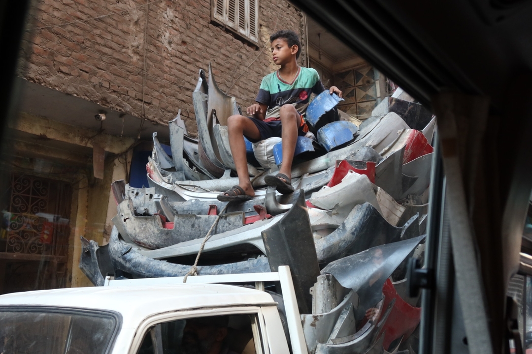 Jeune personne assise sur un tas de pare-chocs de voiture.
