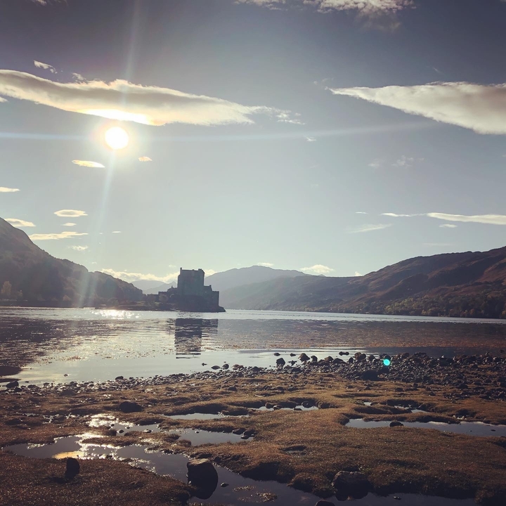 A silhouetted castle by the water under the sun.
