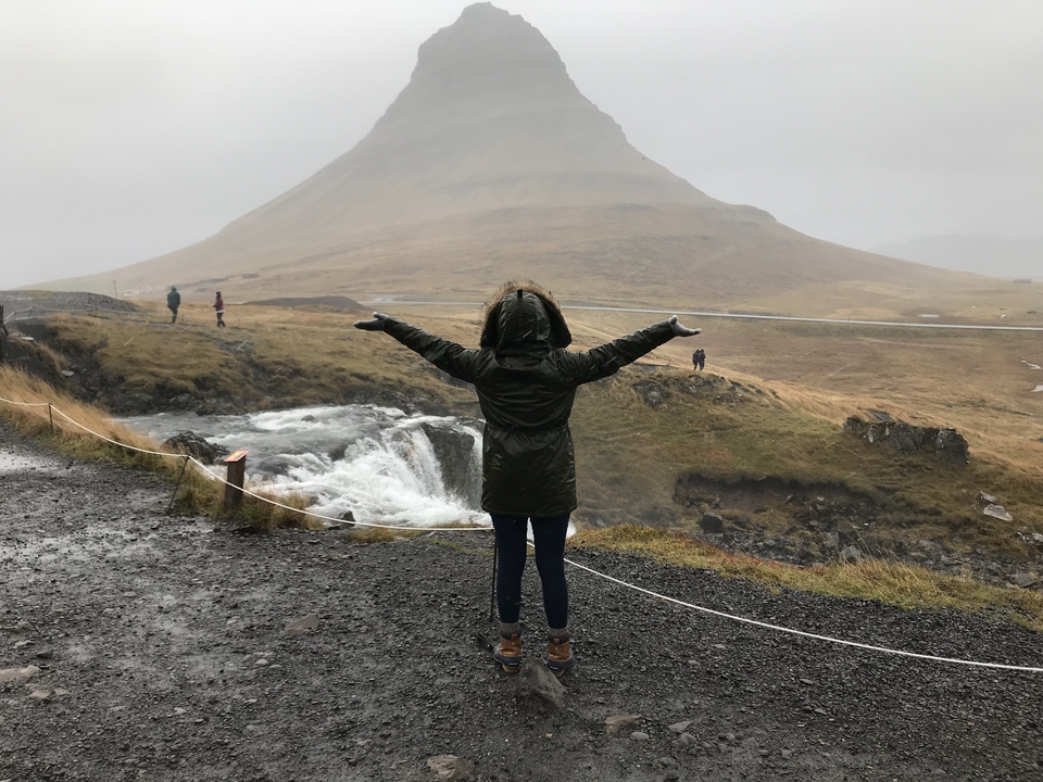 Person with arms raised in front of a mountain.