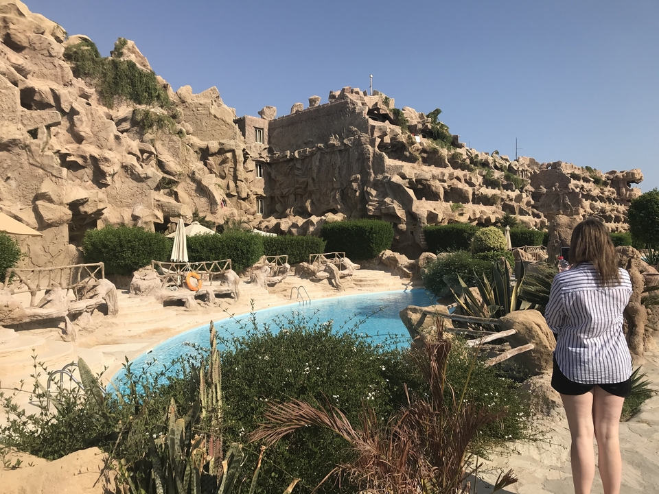Person walking by a pool with unique stone structures.