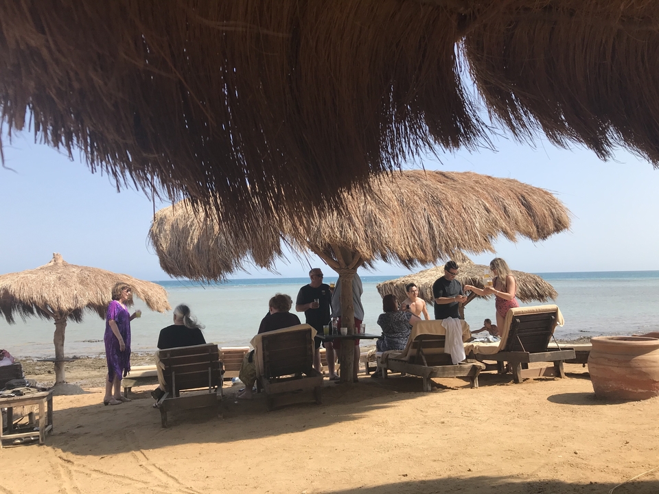 People relaxing under thatched umbrellas by the sea.