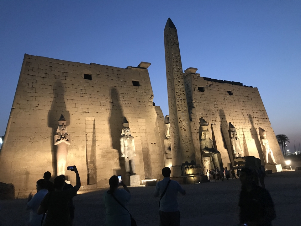 Tourists viewing illuminated ancient Egyptian temple at night.