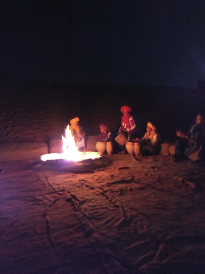 Blurry image of people gathered around a campfire at night.