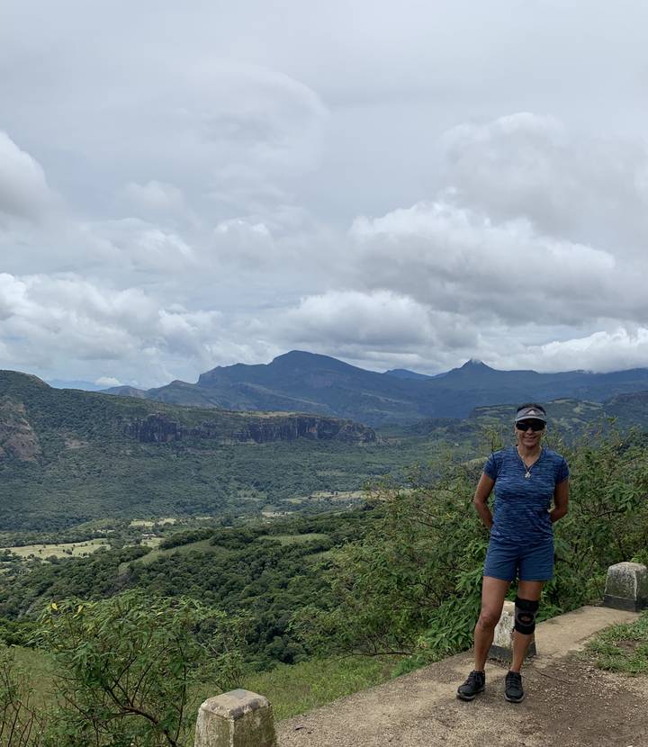 A person standing in a mountainous area with clouds in the background.