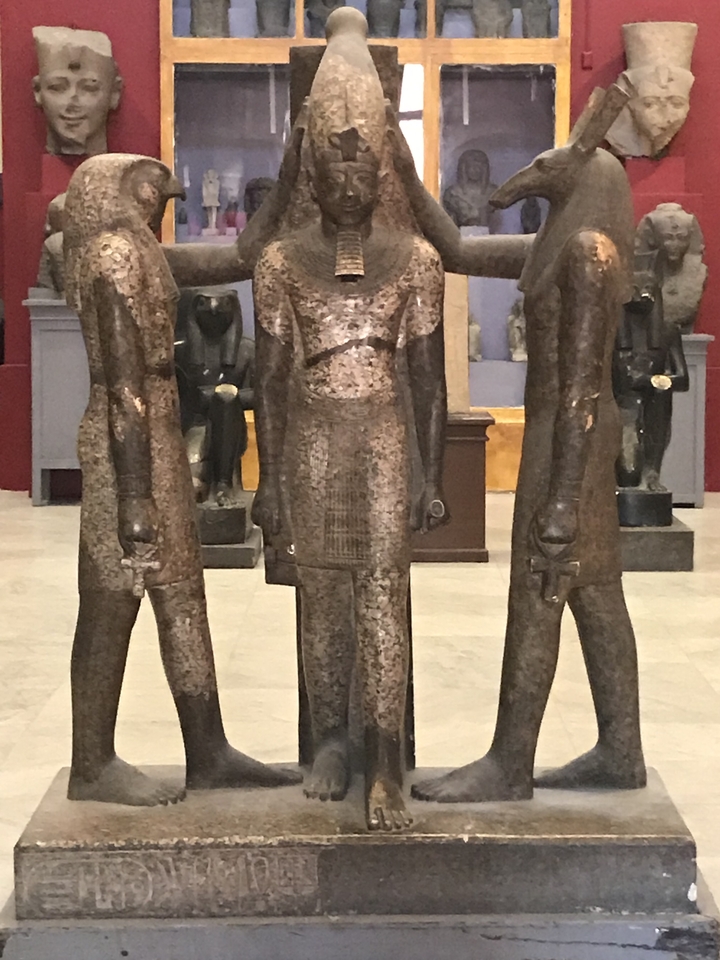 Trois statues de divinités égyptiennes dans un cadre muséal.
