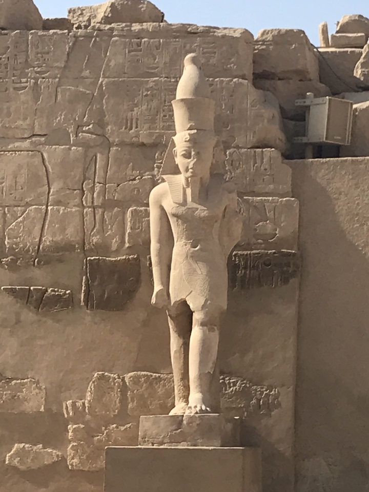 Statue d'un pharaon de l'Égypte antique avec des hiéroglyphes sur le mur.