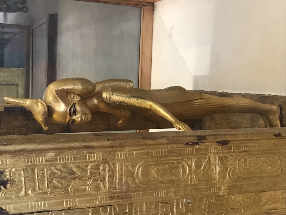 Une figure dorée reposant sur une surface en bois avec des hiéroglyphes.