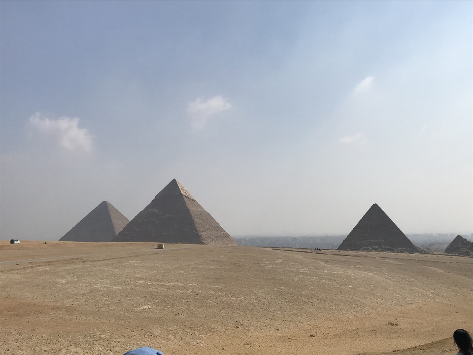 Trois pyramides sur une vaste plaine désertique sous un ciel partiellement nuageux.