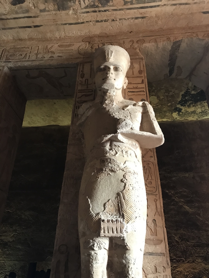 Statue monumentale d'une figure égyptienne à l'intérieur d'un temple faiblement éclairé.