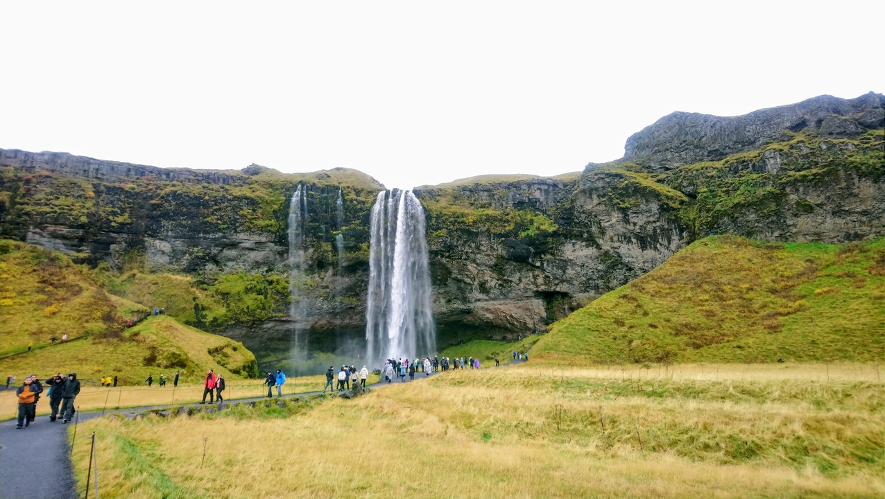Tourists at the foot of a large waterfall.