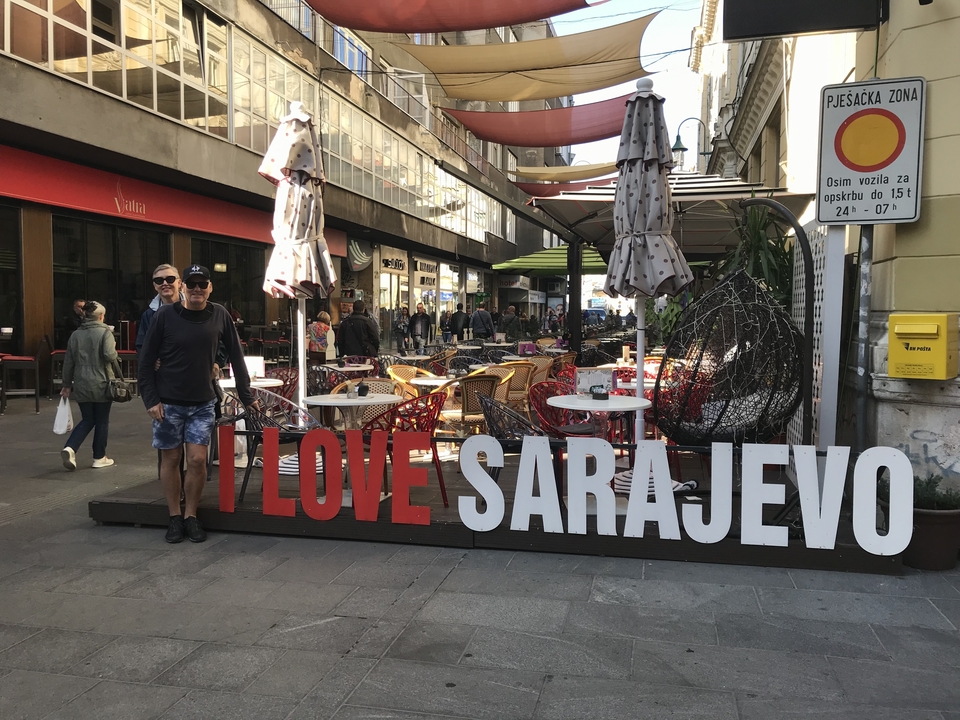 Couple posant à côté d'un panneau « J'aime Sarajevo » dans une rue.