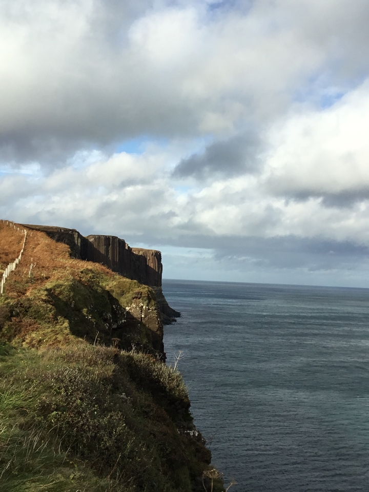 Coastal cliffs overlooking the ocean under a partly cloudy sky.