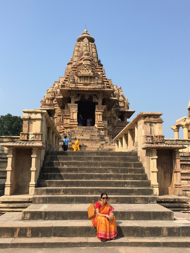 Visitors sitting on temple steps at Khajuraho with decorative carvings.