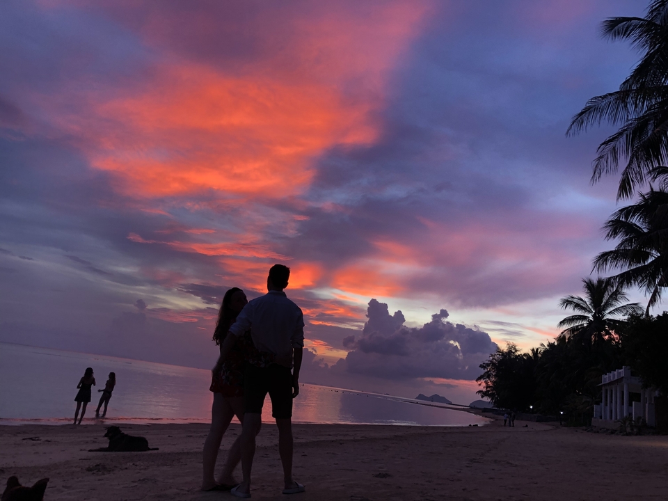Couple standing on a beach during a colorful sunset.