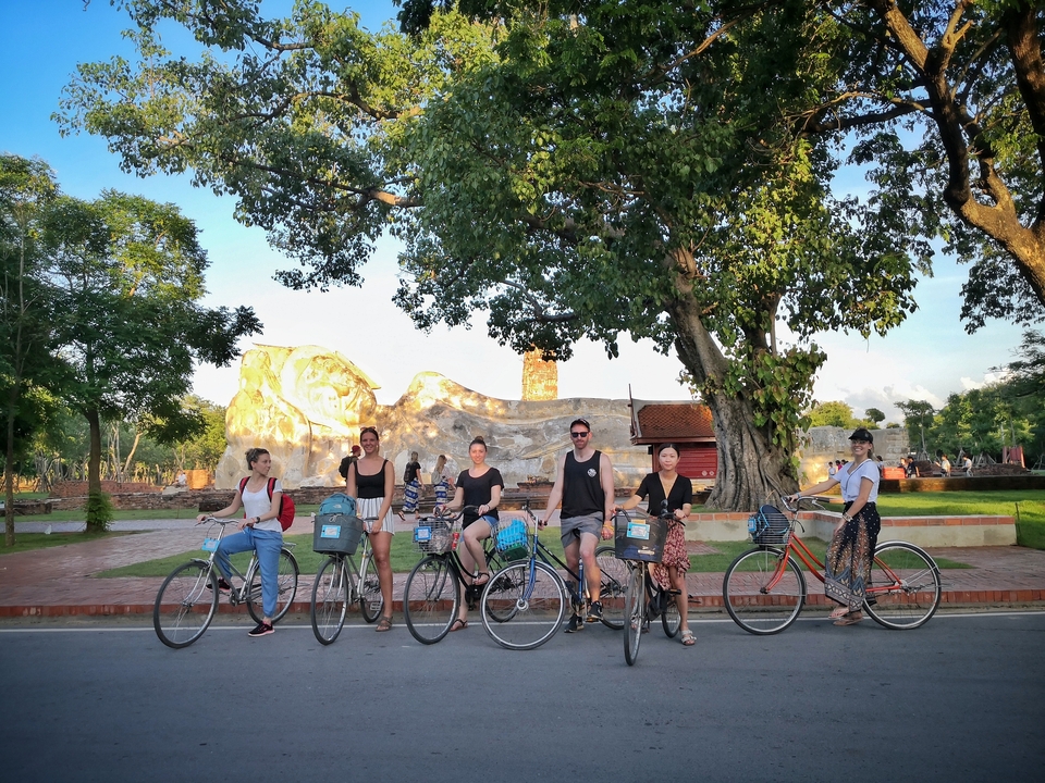 People on bicycles near a reclining Buddha statue.